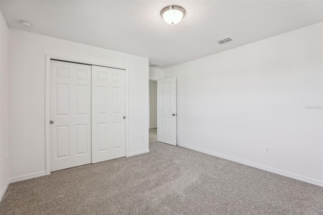 unfurnished bedroom with carpet, baseboards, a textured ceiling, visible vents, and a closet