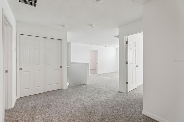 interior space with a closet, a textured ceiling, visible vents, baseboards, and carpet floors