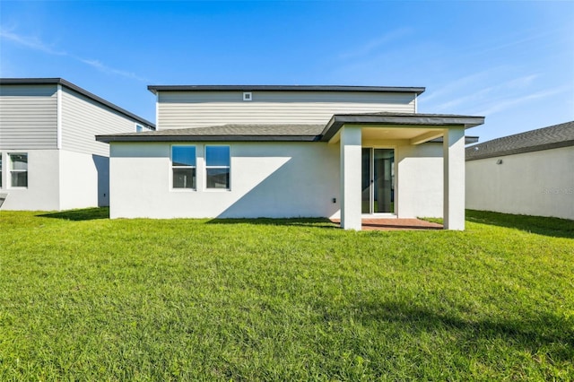 back of house featuring a shingled roof, a lawn, and stucco siding