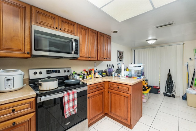 kitchen with appliances with stainless steel finishes, light countertops, brown cabinetry, and a peninsula