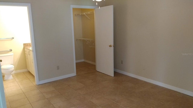 unfurnished bedroom with a closet, a spacious closet, baseboards, and ensuite bathroom