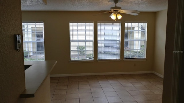 unfurnished dining area featuring a textured ceiling, ceiling fan, plenty of natural light, and baseboards