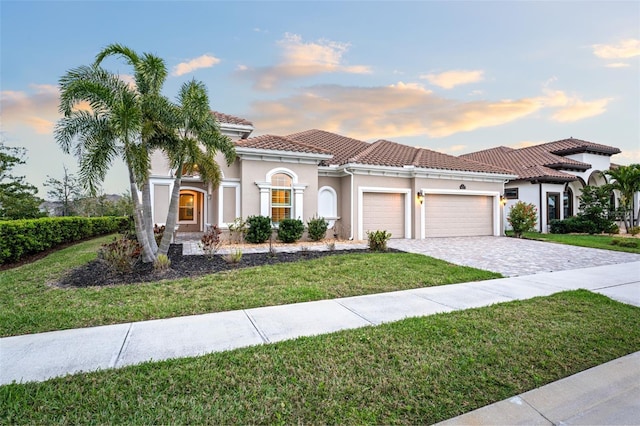 mediterranean / spanish house with stucco siding, a lawn, decorative driveway, a garage, and a tiled roof