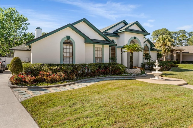 view of front facade featuring a front yard, a chimney, and stucco siding