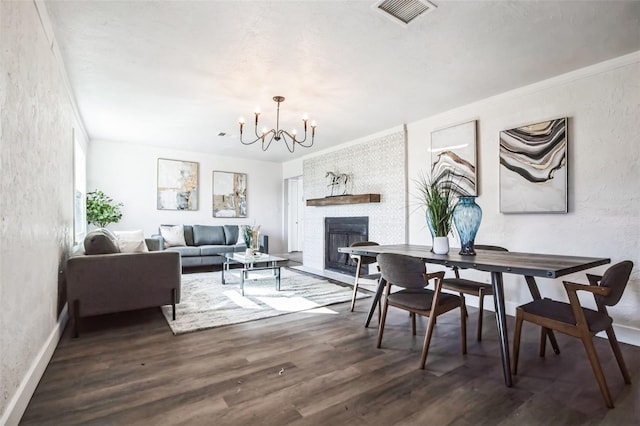 dining space featuring a textured wall, a large fireplace, wood finished floors, visible vents, and an inviting chandelier