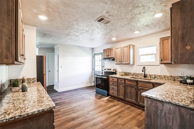 kitchen featuring a textured ceiling, stainless steel appliances, wood finished floors, a sink, and light stone countertops