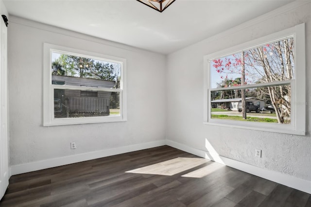 spare room featuring dark wood-style floors, baseboards, and a textured wall