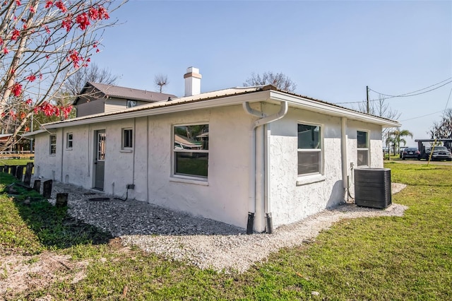 view of home's exterior featuring a yard, central AC unit, a chimney, and stucco siding