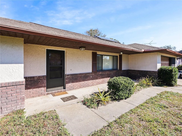 property entrance with solar panels, brick siding, and stucco siding