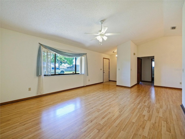 spare room featuring light wood-type flooring, lofted ceiling, visible vents, and a textured ceiling