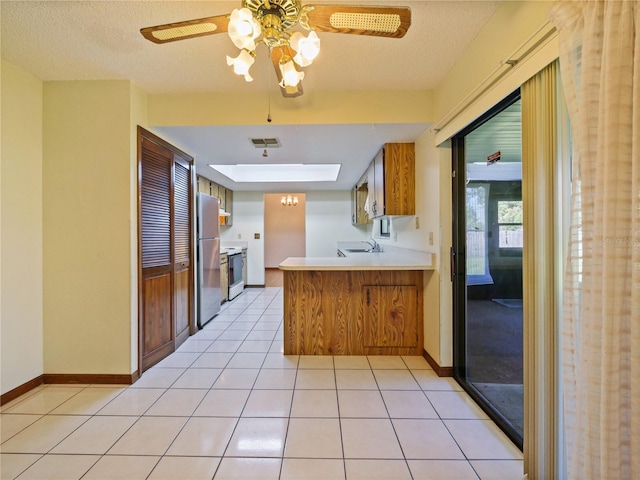 kitchen featuring light tile patterned floors, a peninsula, a sink, visible vents, and freestanding refrigerator