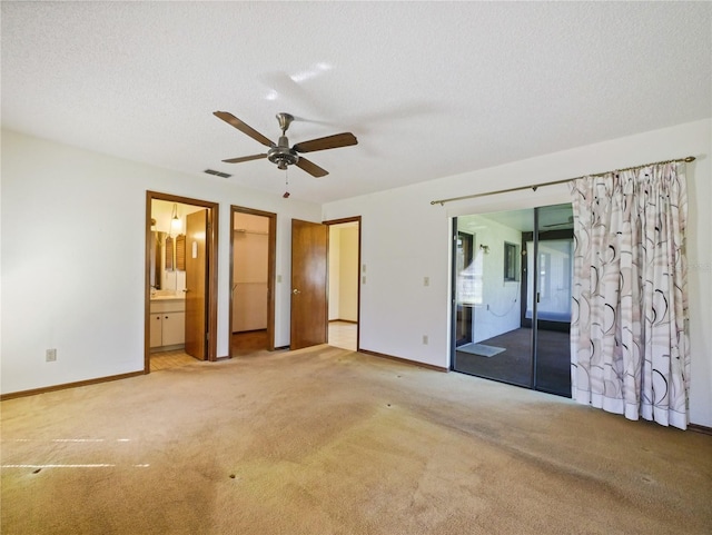 unfurnished bedroom featuring carpet floors, a walk in closet, visible vents, and ensuite bath