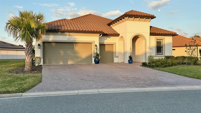 mediterranean / spanish home with an attached garage, a tile roof, decorative driveway, stucco siding, and a front lawn