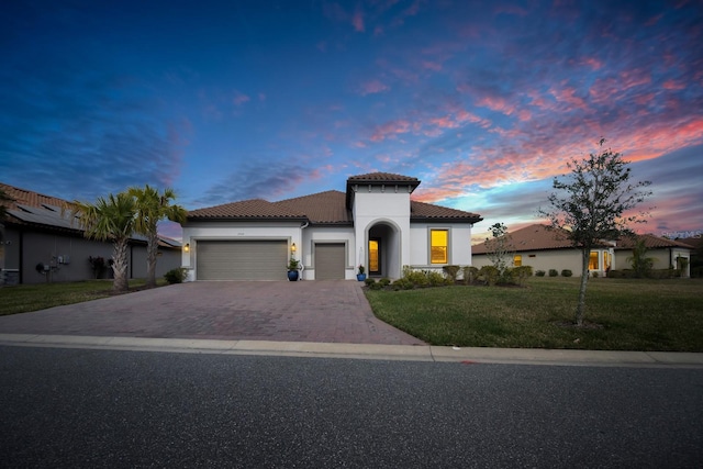 mediterranean / spanish-style home featuring a tiled roof, an attached garage, decorative driveway, a front yard, and stucco siding