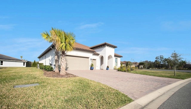 mediterranean / spanish house with a garage, a tile roof, decorative driveway, stucco siding, and a front yard