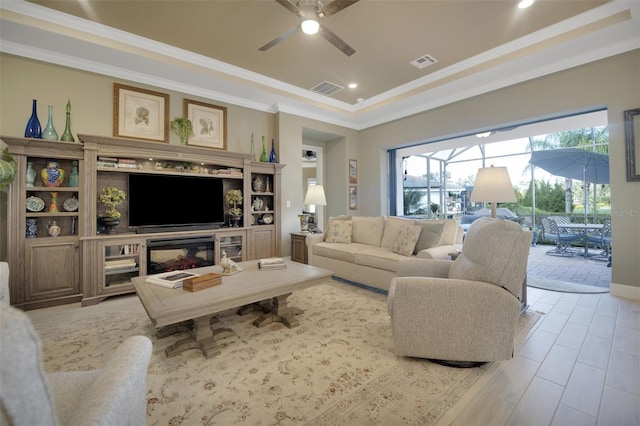 living area with a ceiling fan, visible vents, a raised ceiling, and crown molding