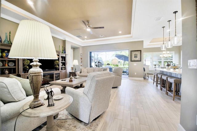 living area featuring ceiling fan with notable chandelier, visible vents, light wood-type flooring, a tray ceiling, and crown molding