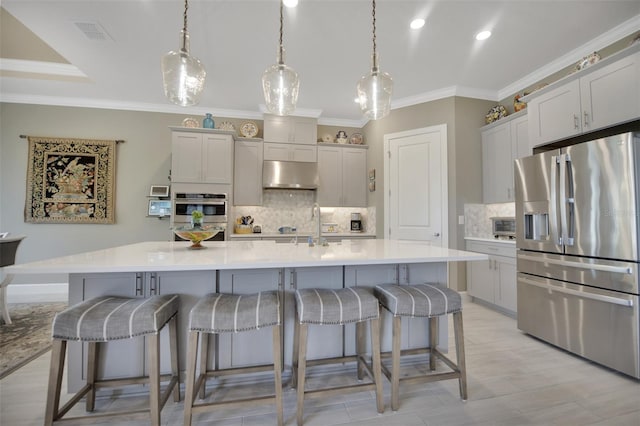 kitchen featuring visible vents, a breakfast bar area, stainless steel appliances, crown molding, and under cabinet range hood