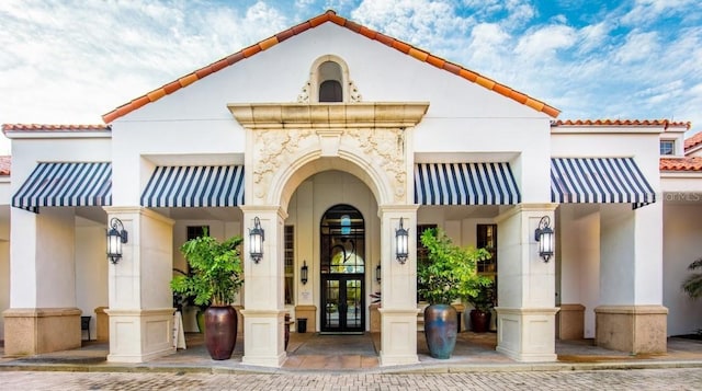 entrance to property with stucco siding, a tiled roof, and french doors