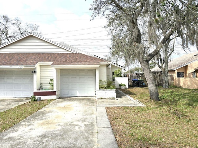 view of property exterior with a garage, concrete driveway, roof with shingles, fence, and a yard