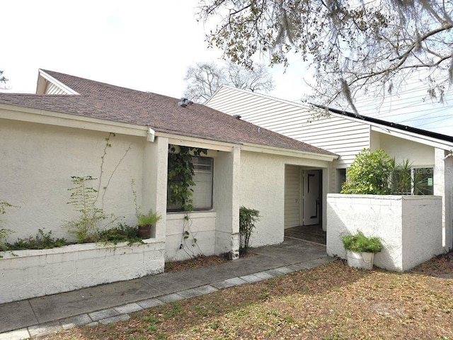 exterior space featuring a shingled roof and stucco siding