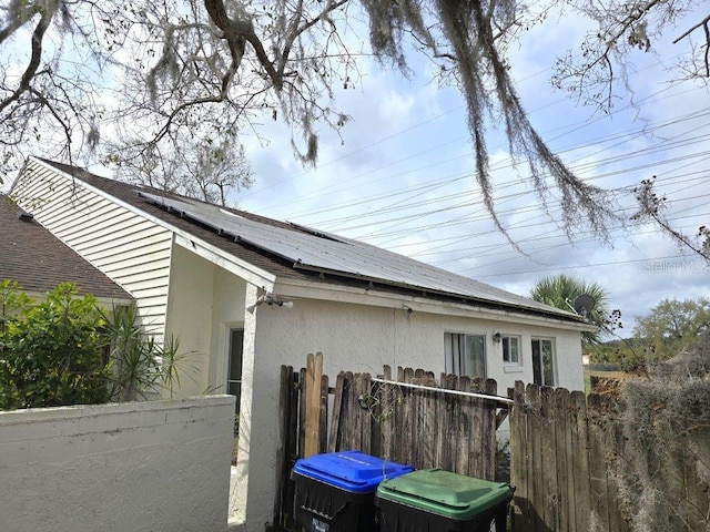 view of side of property featuring roof mounted solar panels, fence, and stucco siding