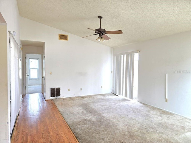 unfurnished room with lofted ceiling, ceiling fan, visible vents, and a textured ceiling