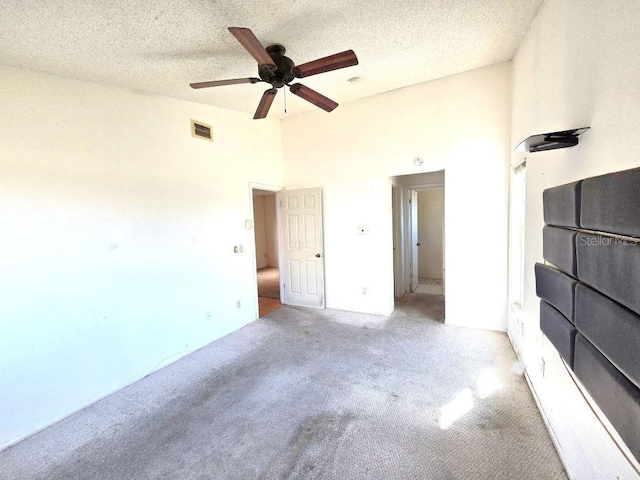 unfurnished bedroom with light carpet, a towering ceiling, visible vents, and a textured ceiling