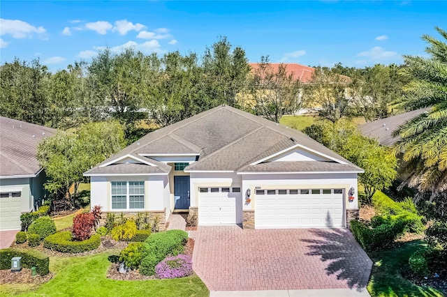 ranch-style house with a garage, stone siding, decorative driveway, and stucco siding