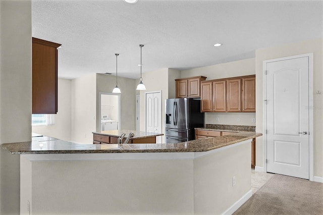 kitchen featuring a center island, light colored carpet, brown cabinetry, dark stone countertops, and stainless steel fridge