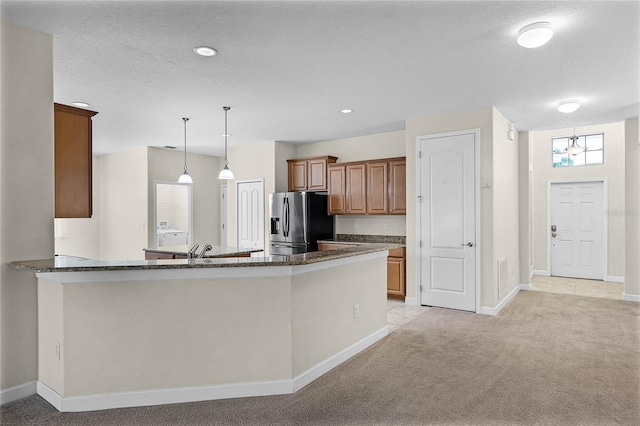 kitchen with brown cabinetry, stainless steel fridge, light carpet, and dark stone countertops