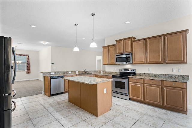 kitchen with appliances with stainless steel finishes, brown cabinetry, a sink, light stone countertops, and a peninsula