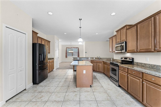 kitchen featuring a peninsula, a sink, appliances with stainless steel finishes, brown cabinets, and decorative light fixtures