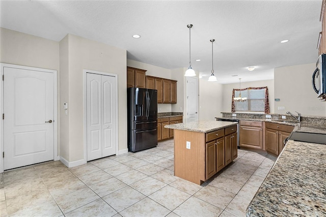 kitchen with light stone counters, a peninsula, a kitchen island, black fridge, and decorative light fixtures