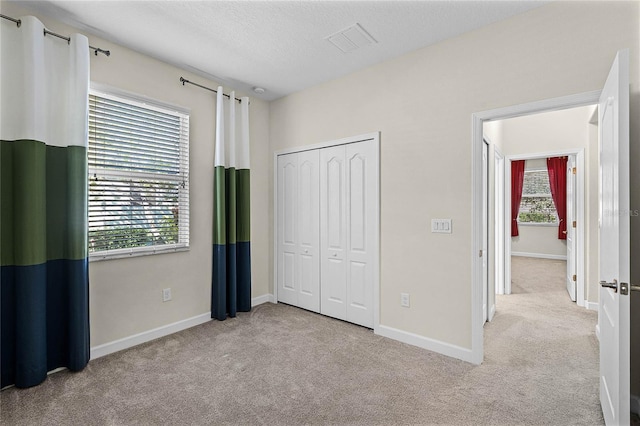 unfurnished bedroom with a closet, visible vents, carpet flooring, a textured ceiling, and baseboards