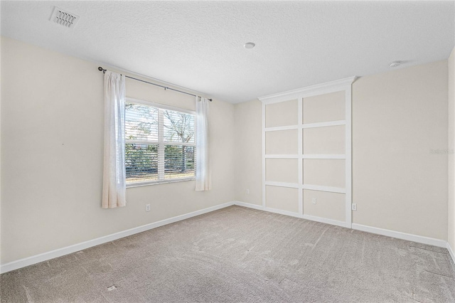 carpeted spare room featuring a textured ceiling, visible vents, and baseboards