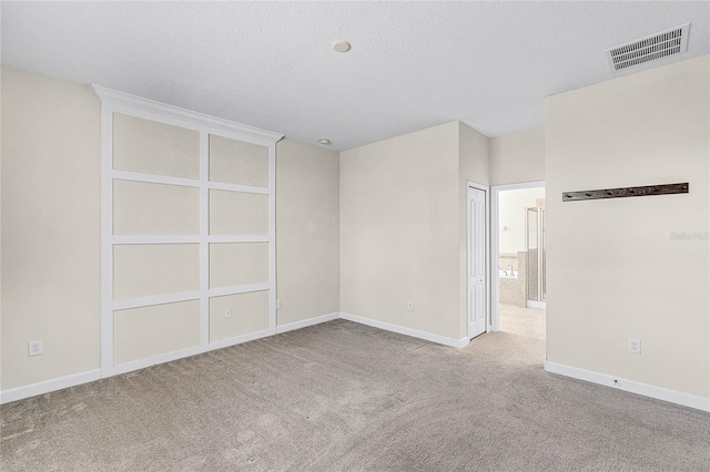 carpeted spare room featuring baseboards, visible vents, and a textured ceiling