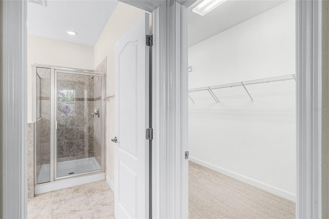 full bath featuring a textured ceiling, baseboards, a spacious closet, tile patterned floors, and a stall shower