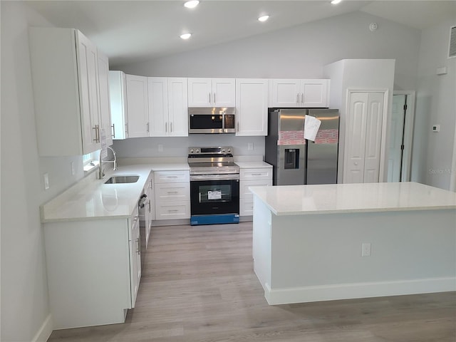 kitchen with appliances with stainless steel finishes, vaulted ceiling, white cabinetry, and a sink