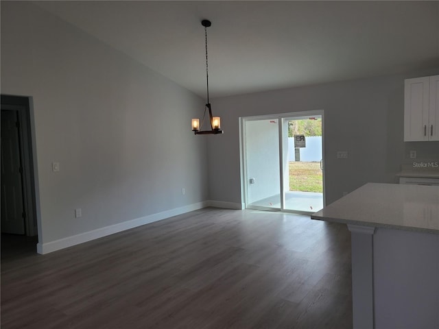 unfurnished dining area featuring dark wood-style floors, a chandelier, vaulted ceiling, and baseboards