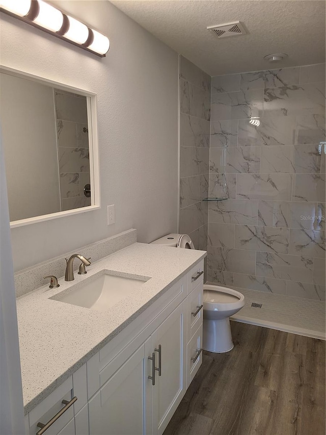 bathroom featuring a textured ceiling, wood finished floors, vanity, visible vents, and a stall shower