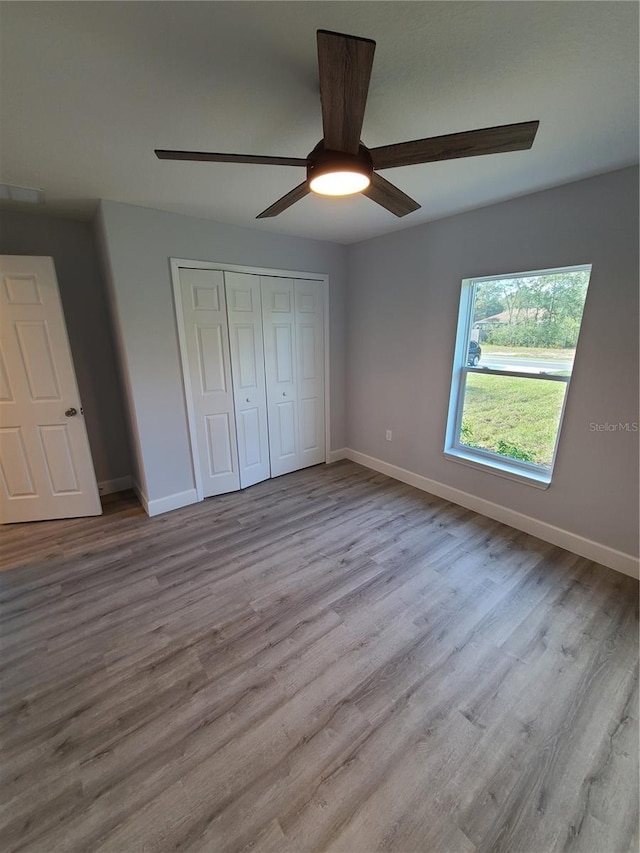 unfurnished bedroom with light wood-style floors, a closet, ceiling fan, and baseboards