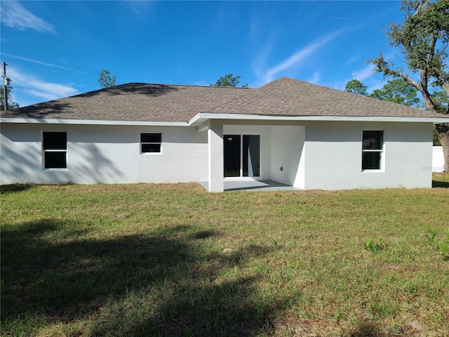 back of house with a shingled roof, a lawn, and stucco siding