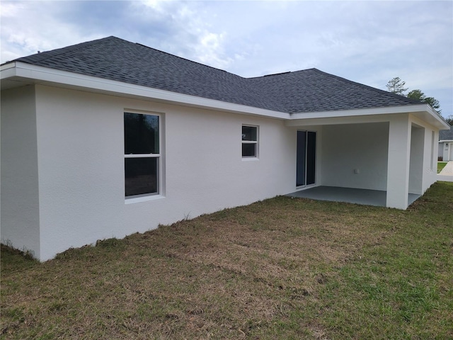 back of property featuring a patio area, a shingled roof, a lawn, and stucco siding