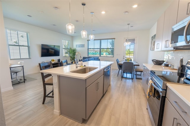 kitchen with appliances with stainless steel finishes, open floor plan, a sink, gray cabinets, and backsplash