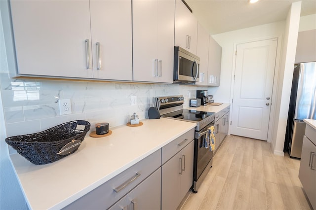 kitchen featuring stainless steel appliances, light countertops, backsplash, gray cabinetry, and light wood-style floors