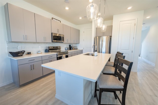 kitchen featuring a breakfast bar, gray cabinets, decorative backsplash, appliances with stainless steel finishes, and a sink