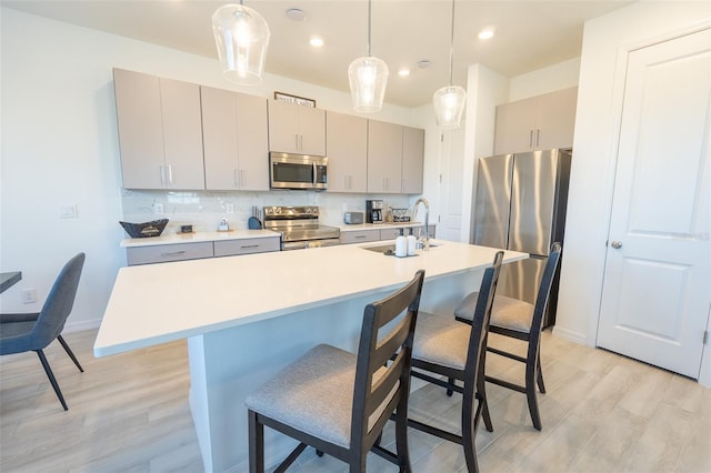 kitchen featuring a breakfast bar area, stainless steel appliances, tasteful backsplash, gray cabinetry, and a sink