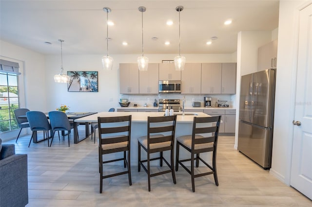 kitchen featuring a breakfast bar area, stainless steel appliances, light countertops, gray cabinetry, and backsplash