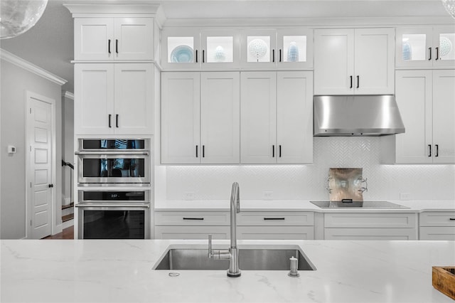 kitchen with crown molding, double oven, white cabinets, a sink, and under cabinet range hood